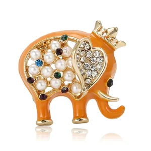 Broche éléphant en émail orange avec couronne dorée, strass colorés et perles sur fond blanc