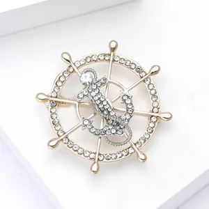Elegant nautical ship wheel and anchor brooch with sparkling rhinestones on white pedestal