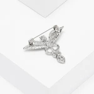 Détail d'une broche caducée argentée ornée de strass brillants sur un support blanc