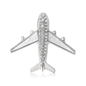 Silver airplane brooch with sparkling rhinestones and white shell wings on white background