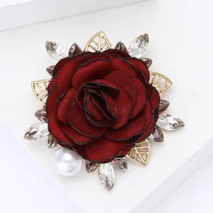 Close-up of deep red fabric rose brooch with golden leaves and sparkling rhinestones