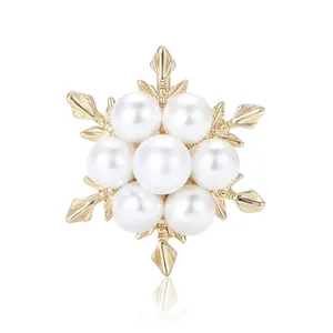 Élégante broche flocon de neige dorée avec sept perles blanches sur une surface blanche