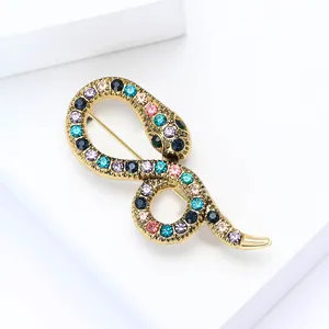 Eleganter goldener Schlangen-Anstecker mit bunten Strasssteinen auf weißem Sockel