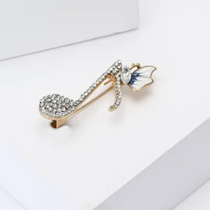 Détail macro de broche note de musique dorée avec strass et ailes en émail bleu