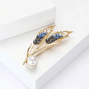 Elegant gold wheat ear brooch with blue crystals and white pearl on a white pedestal