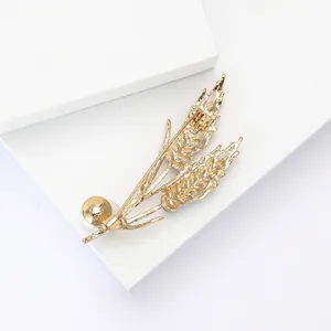Detailed close-up of a golden wheat stalk brooch with an elegant white pearl accent