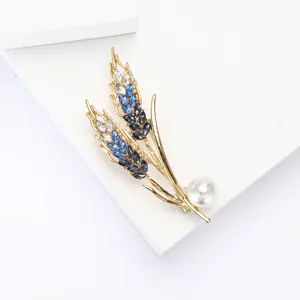 Detailed close-up of golden wheat ear brooch with blue crystals and a white pearl