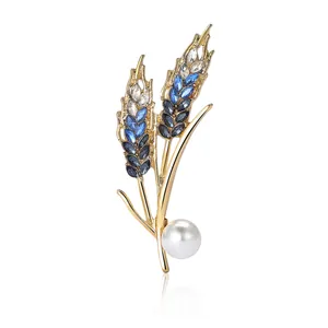 Elegant gold wheat brooch with blue crystals and a large pearl on white background