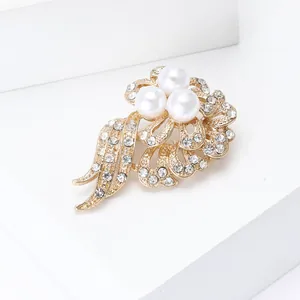 Elegant gold flower brooch with white pearls and rhinestones on a white pedestal