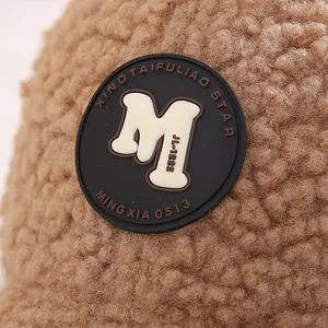 Makroansicht des hellbraunen Plüschstoffs mit dem strukturierten M-Logo auf der Kindermütze
