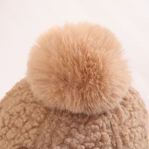 Close-up of children's winter hat featuring thick brown faux fur and fluffy pompom detail