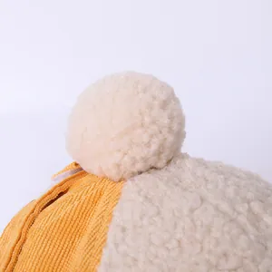 Macro detail of yellow corduroy fabric with white faux shearling lining and plush pompom