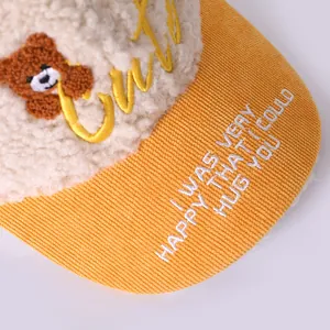 Detailed close-up of yellow corduroy brim and white fleece with teddy bear embroidery