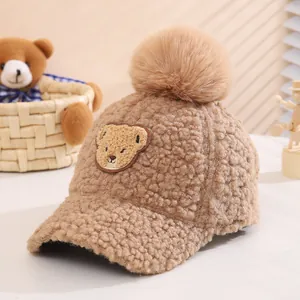 Detailed plush texture of brown kids winter baseball cap with bear patch and pom-pom