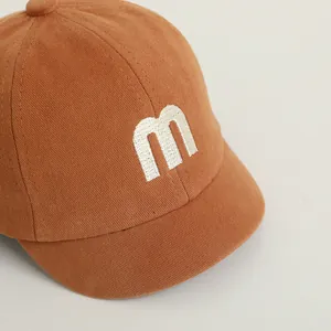 Detail of baby baseball cap showing brown twill cotton fabric and white letter M embroidery