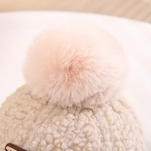 Detailansicht des rosa Kunstfellbommel und beigen Lammwollstoffes einer warmen Wintermütze