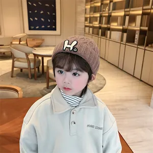 Close-up of brown knit beanie with H-letter patch and cream collared sweatshirt for kids