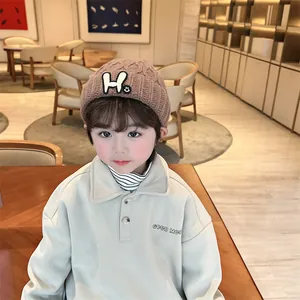 Detail of kids brown knit beanie with H letter patch and beige polo sweatshirt embroidery