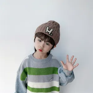 Detail of child wearing a brown knit beanie with H patch and striped sweater
