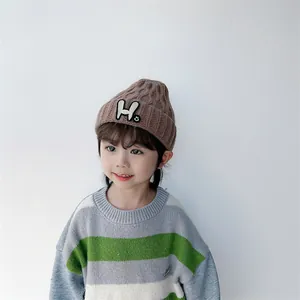 Close-up of brown knit beanie showing detailed vertical willow leaf pattern and H patch