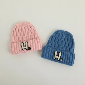 Close-up of pink and blue knit beanies featuring white H embroidery and a smiley face