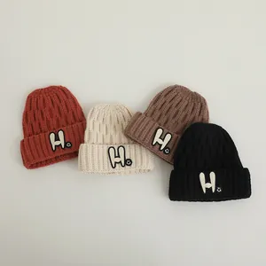 Close-up of knit beanies in four colors with H-letter patches and smiley embroidery