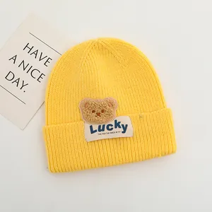 Dettaglio macro del berretto in maglia giallo con toppa orso e etichetta Lucky