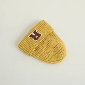 Detail einer gelben Strickmütze für Babys mit braunem R-Aufnäher und weicher Wollstruktur