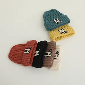 Close-up of six winter knit beanies in various colors featuring H letter smile patches