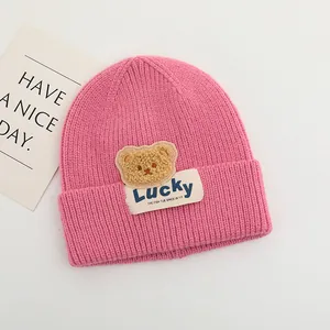 Dettaglio del berretto in maglia rosa per neonati con toppa a orsetto e etichetta Lucky