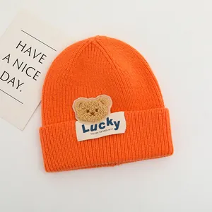 Dettaglio della maglia del cappello arancione con orsetto e etichetta Lucky cucita