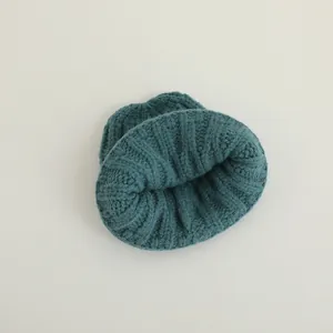 Detail of teal knit winter hat showing thick cable stitch texture and warm rolled edge
