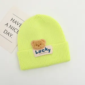 Dettaglio del cappello in maglia a coste verde neon con orsetto e etichetta Lucky