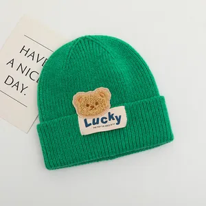 Dettaglio del berretto in maglia verde con orsetto di peluche e toppa ricamata Lucky