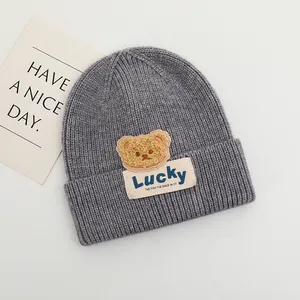 Dettaglio del cappello in maglia grigio scuro con trama a costine e toppa Lucky