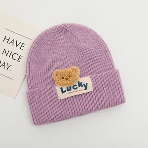 Dettaglio del berretto in maglia viola per neonati con toppa a orsetto e etichetta Lucky