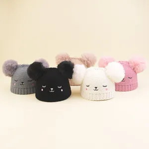 Detail view of five soft knit baby hats with pom-poms and embroidered cat faces