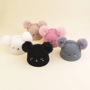 Detail of five infant knitted beanies with double pom-poms and cute cartoon embroidery