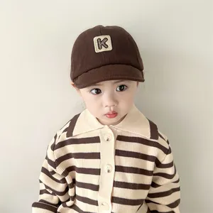 Detail of dark brown corduroy texture and beige 'K' letter patch on a baby baseball cap