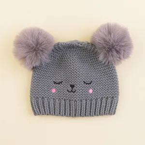 Close-up of winter knit baby hat with large fluffy pom-poms and cute animal face embroidery