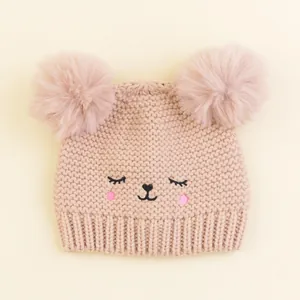 Close-up of baby knit hat featuring soft pink yarn, dual pom-poms, and cute embroidery