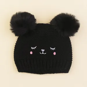 Close-up of black knit baby hat with dual faux fur pom poms and cute cat embroidery