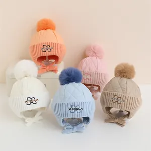 Dettaglio di cappelli in maglia per neonati con paraorecchie, pompon e ricamo a M