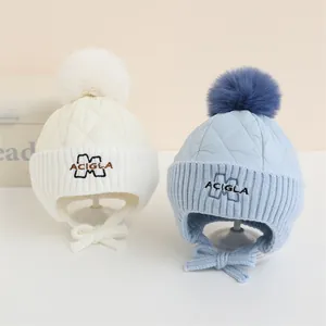 Dettaglio dei cappelli invernali per neonati in crema e blu con pompon e ricamo della M