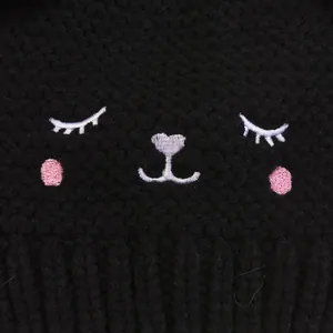 Macro detail of cute cat embroidery on black knitted winter hat for children