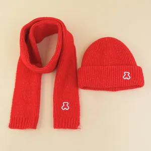 Detail of red knitted winter hat and scarf set featuring cute white bear embroidery