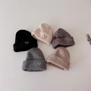 Mise à plat de bonnets tricotés pour bébé en cinq couleurs avec détail de cœur brodé
