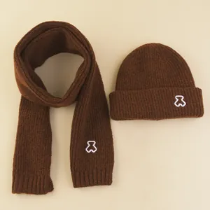 Detail of dark brown knitted hat and scarf set featuring cute bear embroidery and ribbed texture