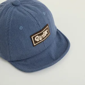 Detail showing the textured blue corduroy fabric and K letter patch on baby baseball cap
