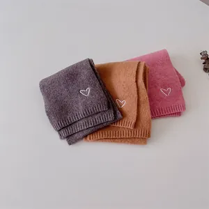 Détail d'écharpes tricotées pour bébé en violet, orange et rose avec broderie cœur